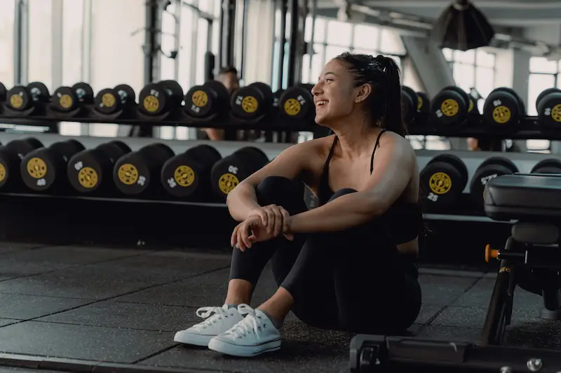 Woman resting in a gym near weights, representing gym membership savings and the Vitality discount